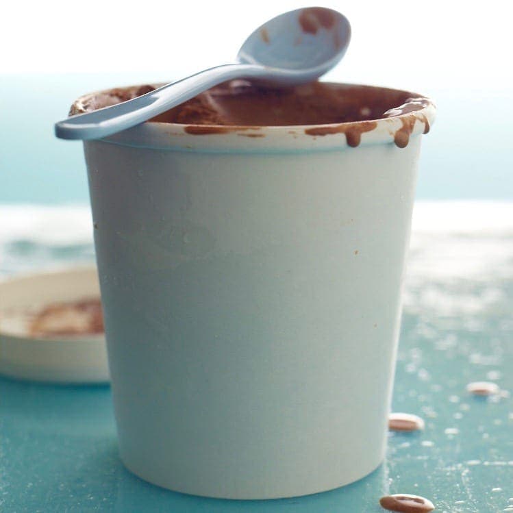 Homemade Chocolate Ice Cream in white paper tub with resting spoon