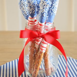 Red, white and blue dipped stick pretzels stand in a jar by an American Flag