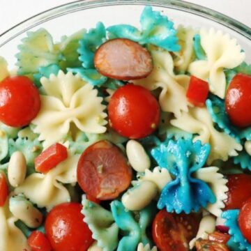 pasta salad with white and blue pasta, red cherry tomatoes and chorizo in a glass bowl