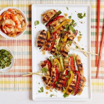 grilled Korean BBQ Chicken with bowls of toppings and red chopsticks