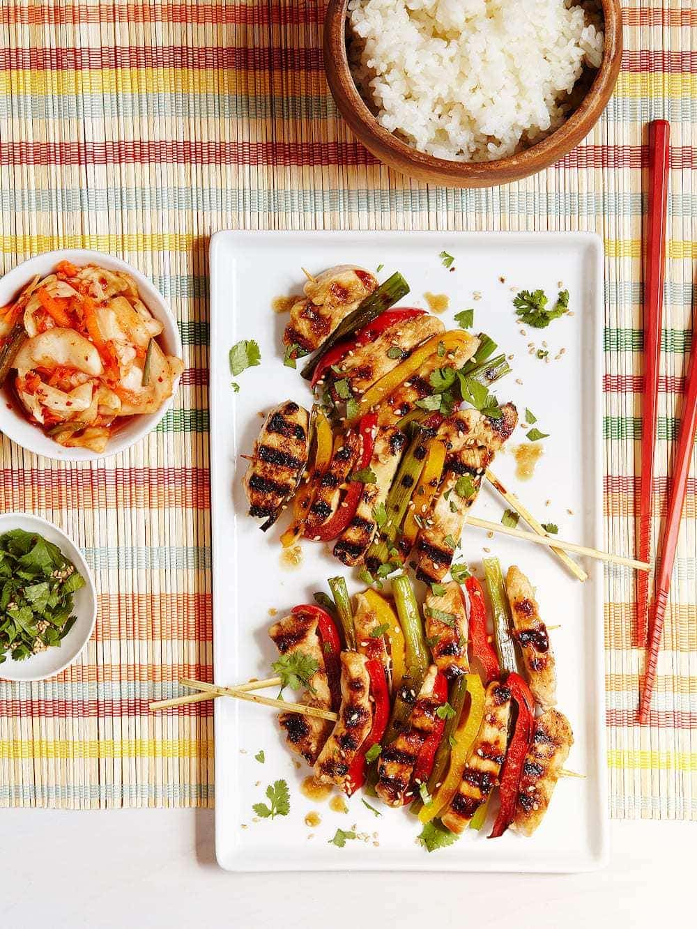 Korean BBQ Chicken Skewers with veggies on rectangular white plate with chopsticks. 