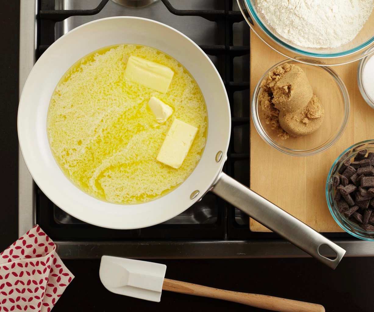 An overhead view of butter being melted in a skillet. More ingredients needed to make the cast iron chocolate chip cookie rest nearby. 