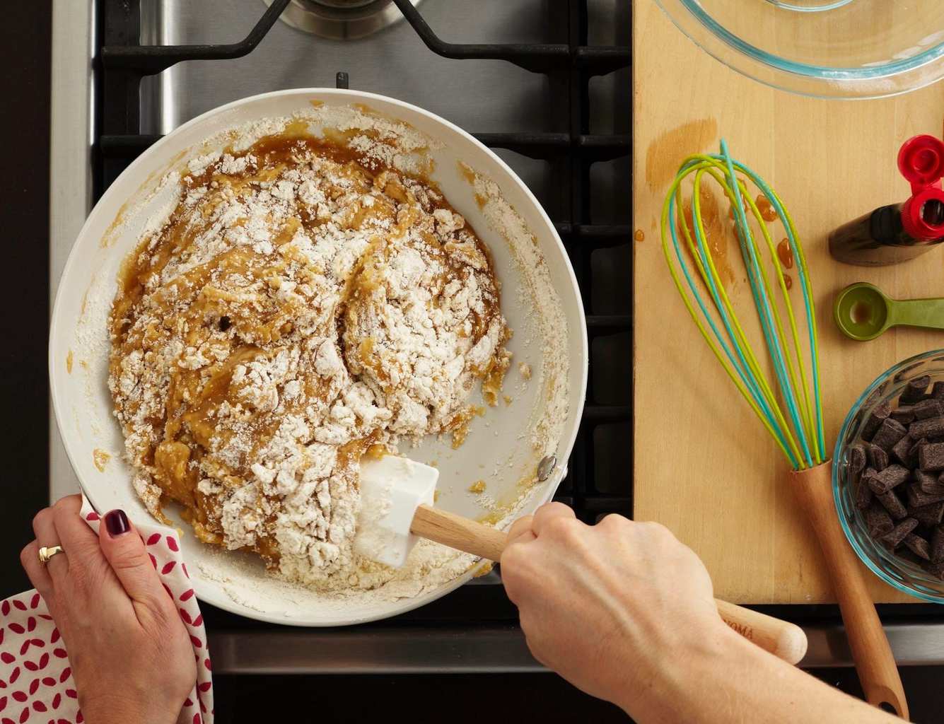 An overhead view of chocolate chip cookie dough being stirred together in a skillet. 