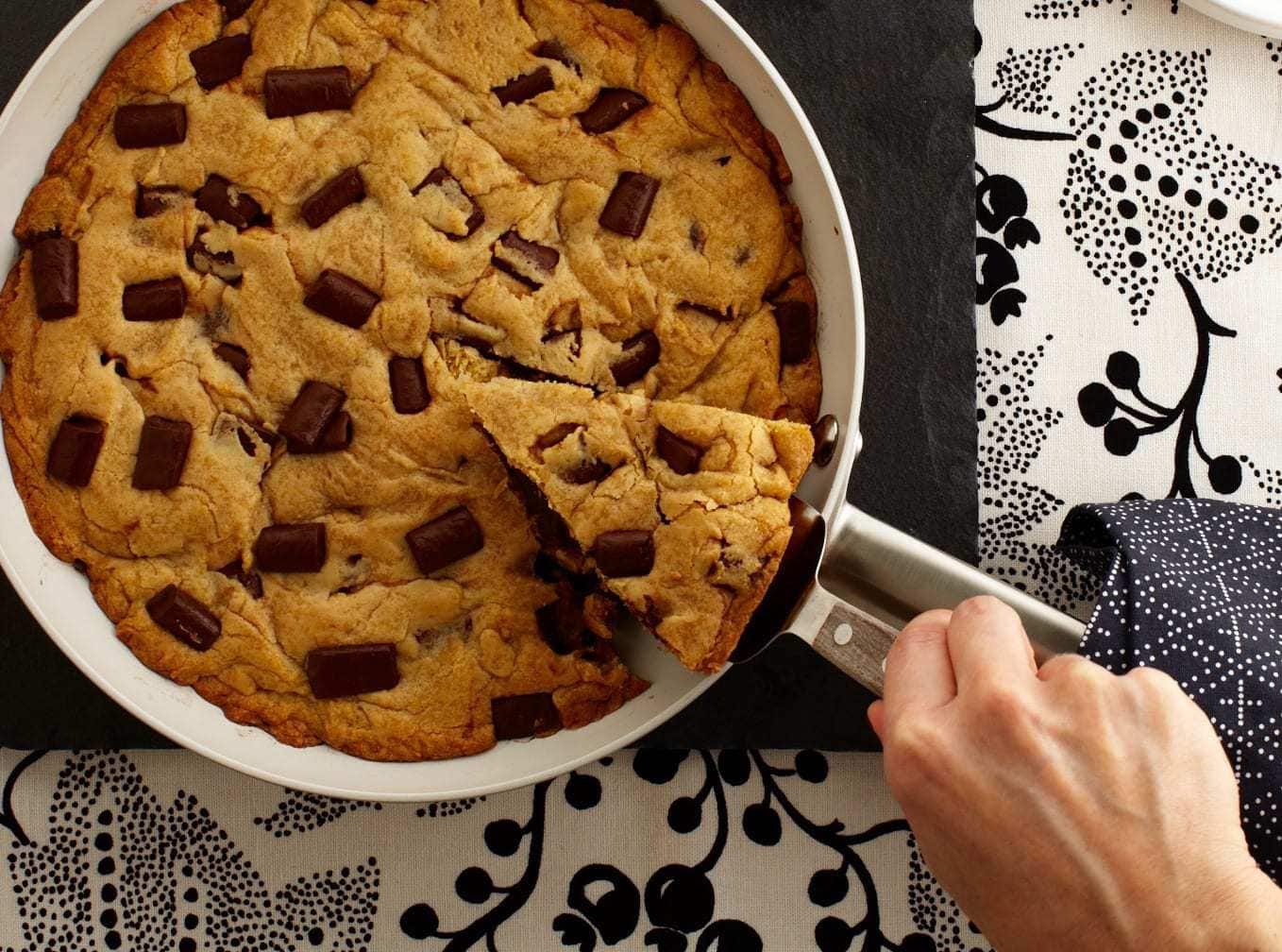 A slice being removed from a skillet cookie, seen from above. 
