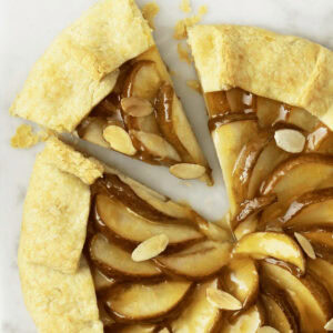 Close up of a pear crostada with a slice cut and slightly removed from the rest of the tart.