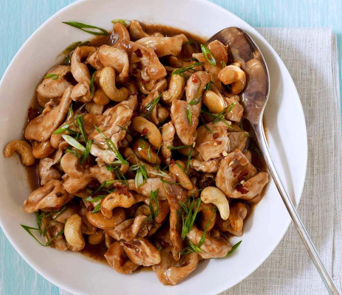 Chinese cashew chicken stir fry with nuts in a white bowl with a spoon