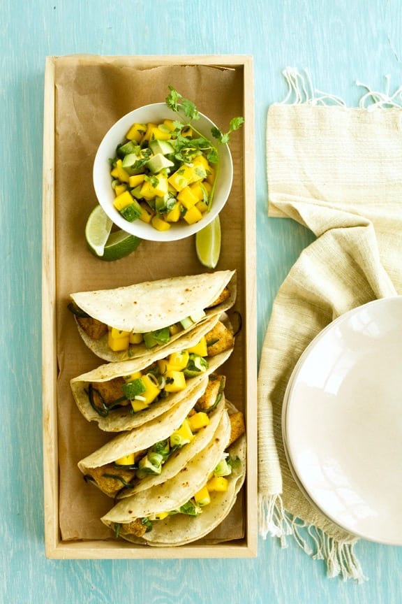 fish tacos with mango and avocado salsa on a blue table