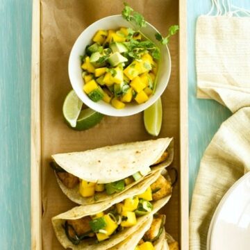 fish tacos with mango and avocado salsa on a blue table