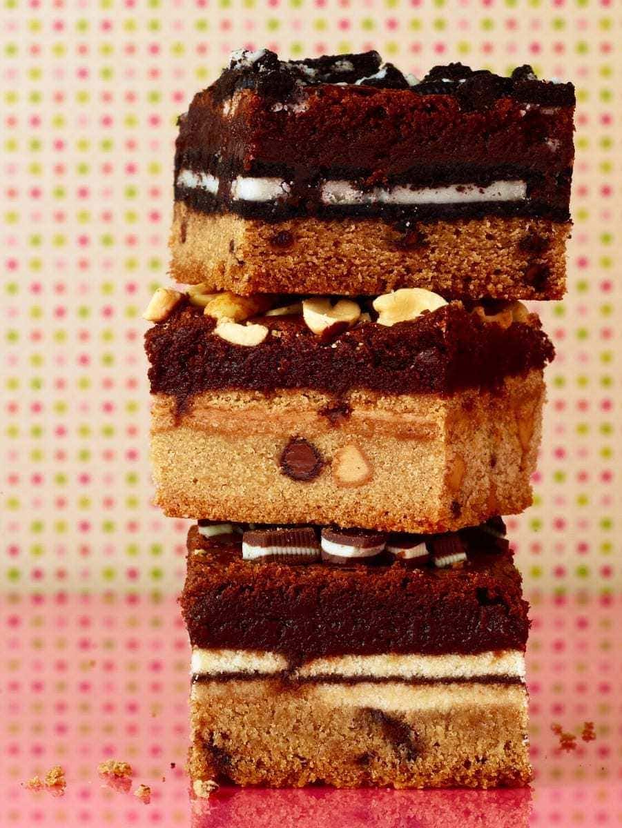 The ultimate cookie stuffed brownies squares stacked on pink surface