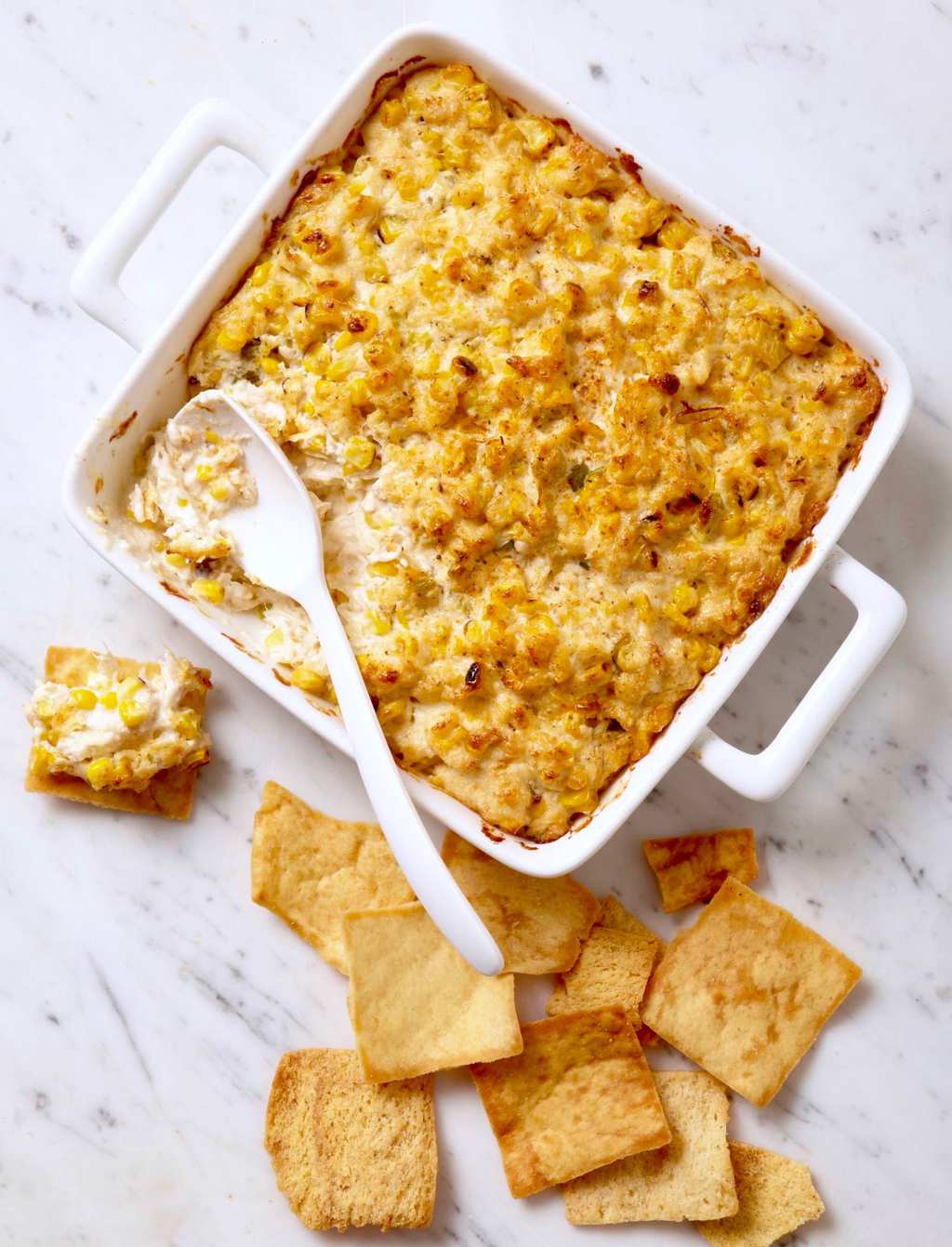 Grilled corn and crab dip in square, white casserole dish, white spoon and chips