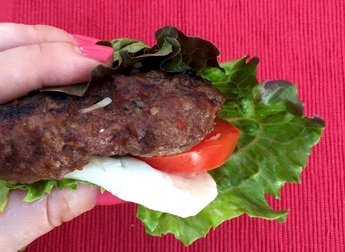 Burger assembled in lettuce wrap with red background.