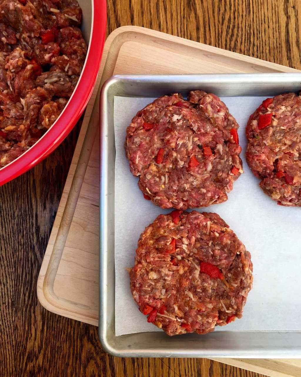 Burger patties on quarter sheet pan and red bowl
