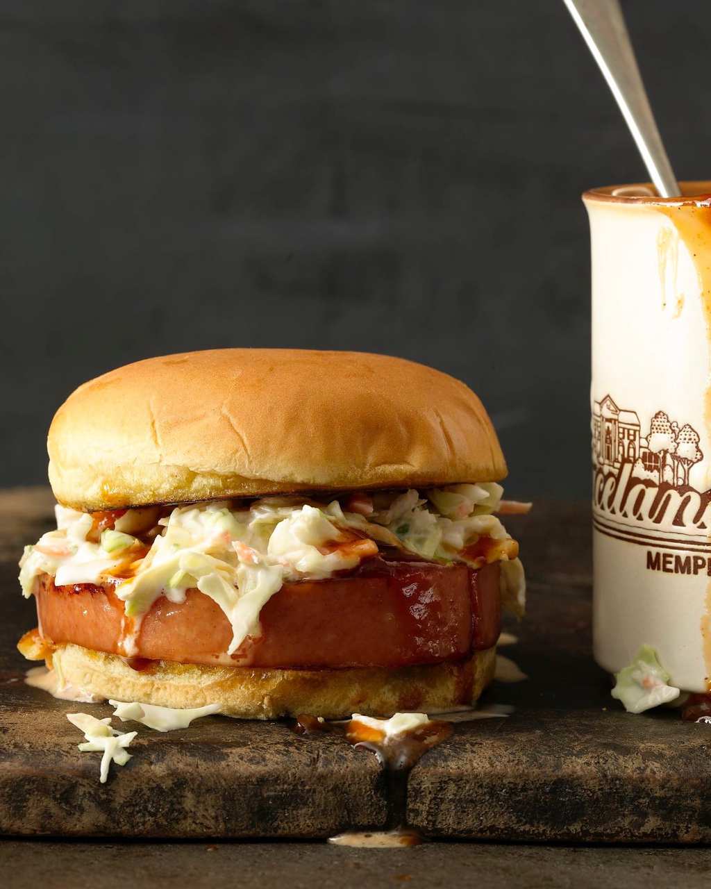 A smoked bologna sandwich topped with coleslaw and bbq sauce. 