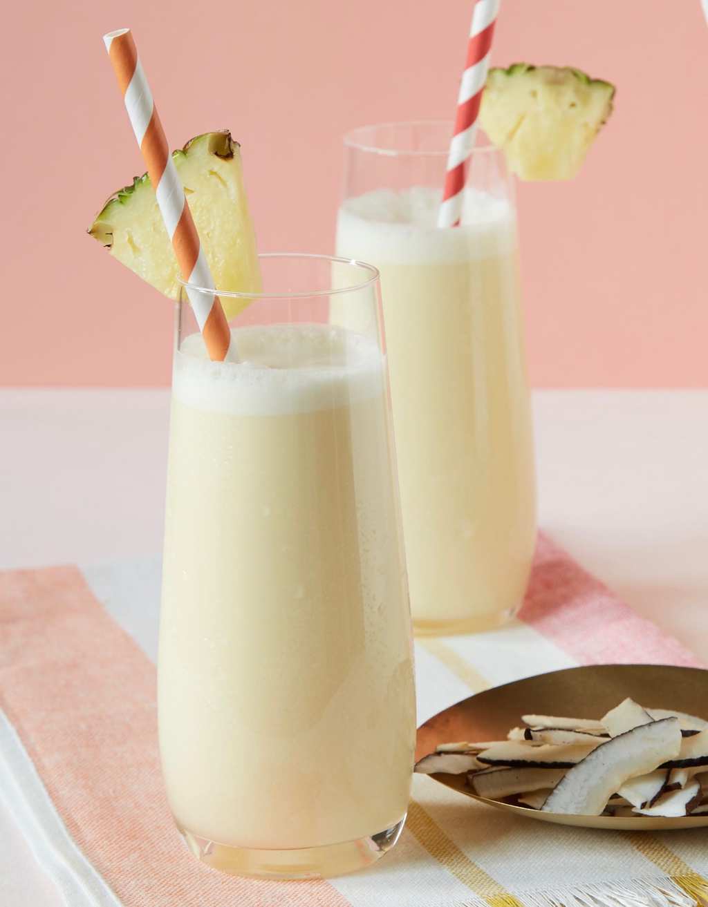 Two creamy pina coladas in tall glasses, garnished with straws and pineapple wedges. 