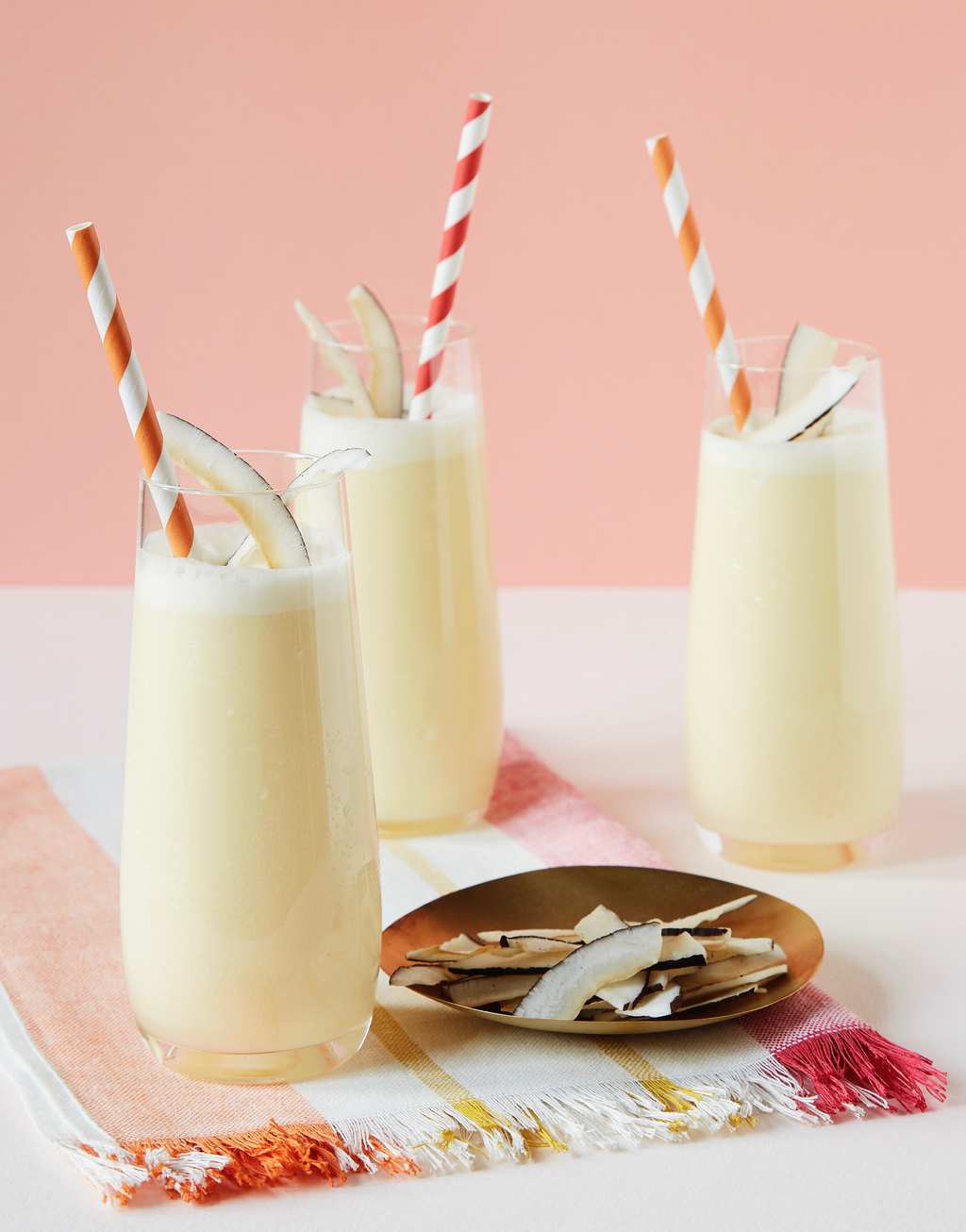 Three homemade pina coladas in tall glasses, garnished with straws and coconut strips. 