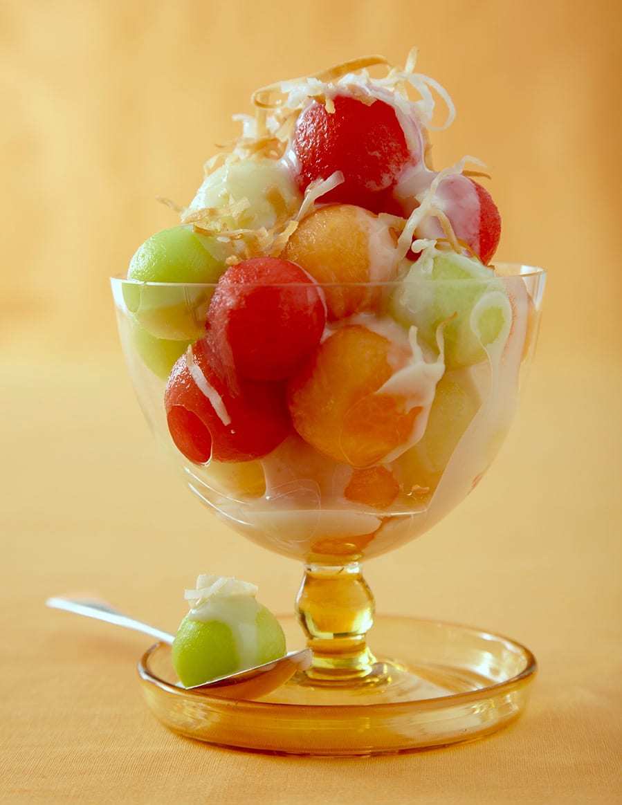 Summer melon dessert with coconut sauce in footed glass with sauce on yellow background