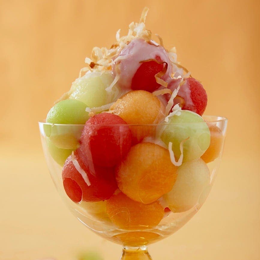 Summer melons and coconut sauce on yellow background in a clear dessert goblet