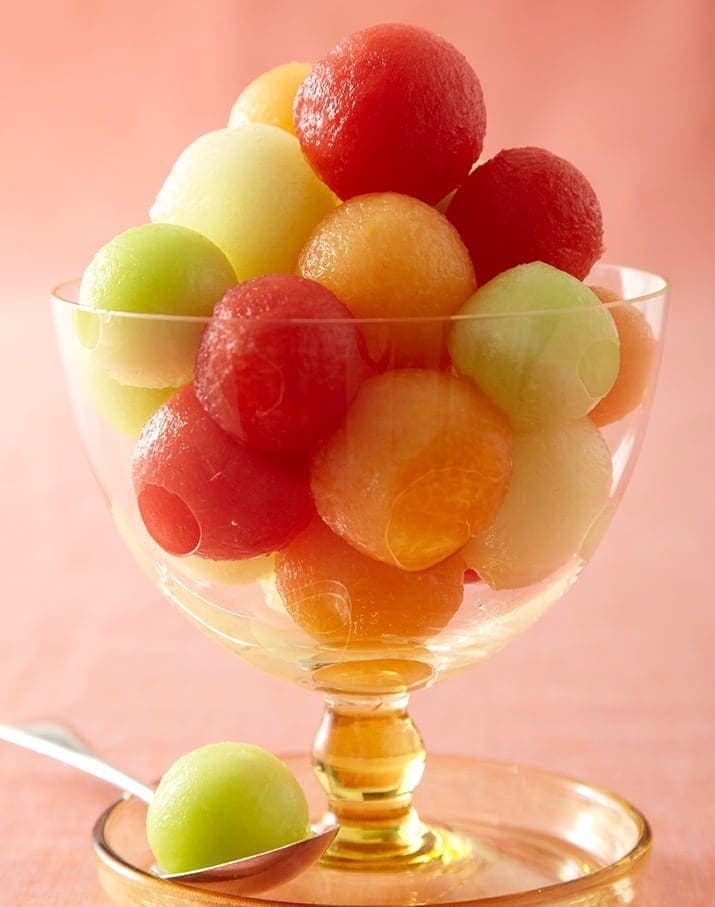 Summer melon dessert with coconut sauce in footed glass, close crop