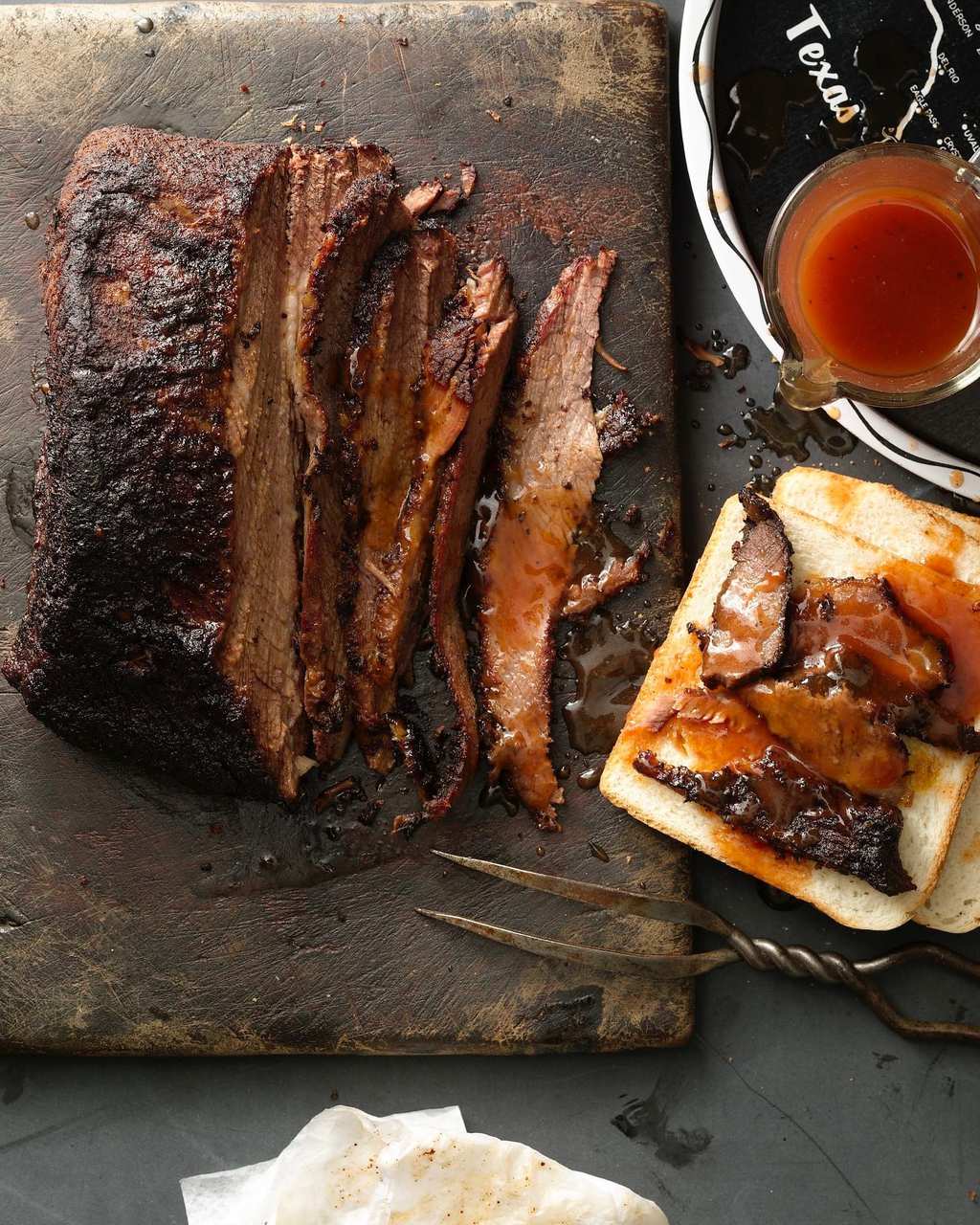 Sliced brisket on rustic board and toast with sauce on the side