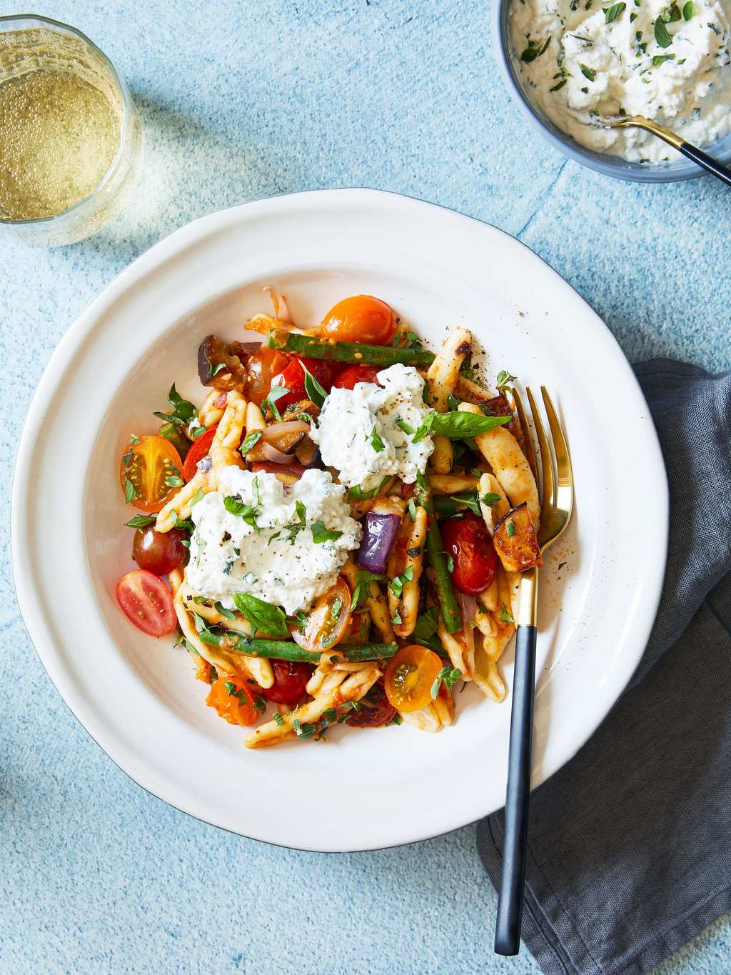 Italian tomato and eggplant skillet pasta in white bowl with fork on blue background