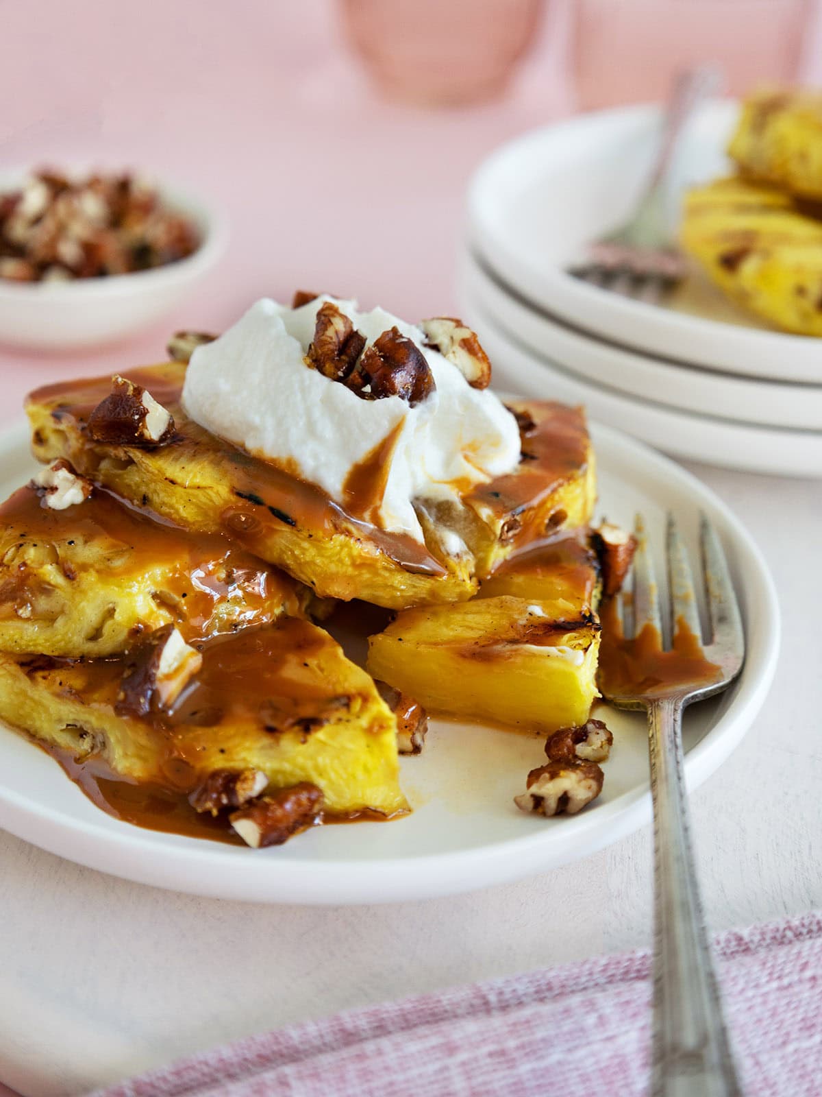 Grilled pineapple topped with caramel and whipped cream on a white plate next to a fork.