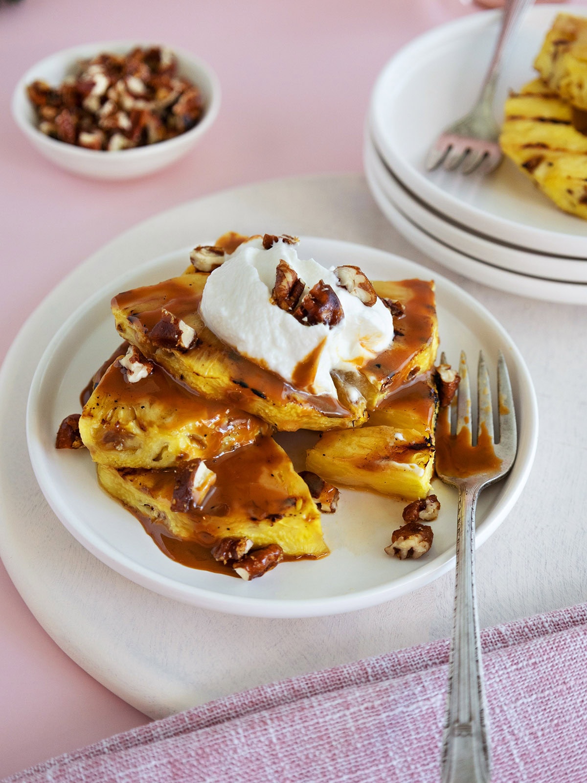 Grilled pineapple topped with caramel and whipped cream on a white plate.