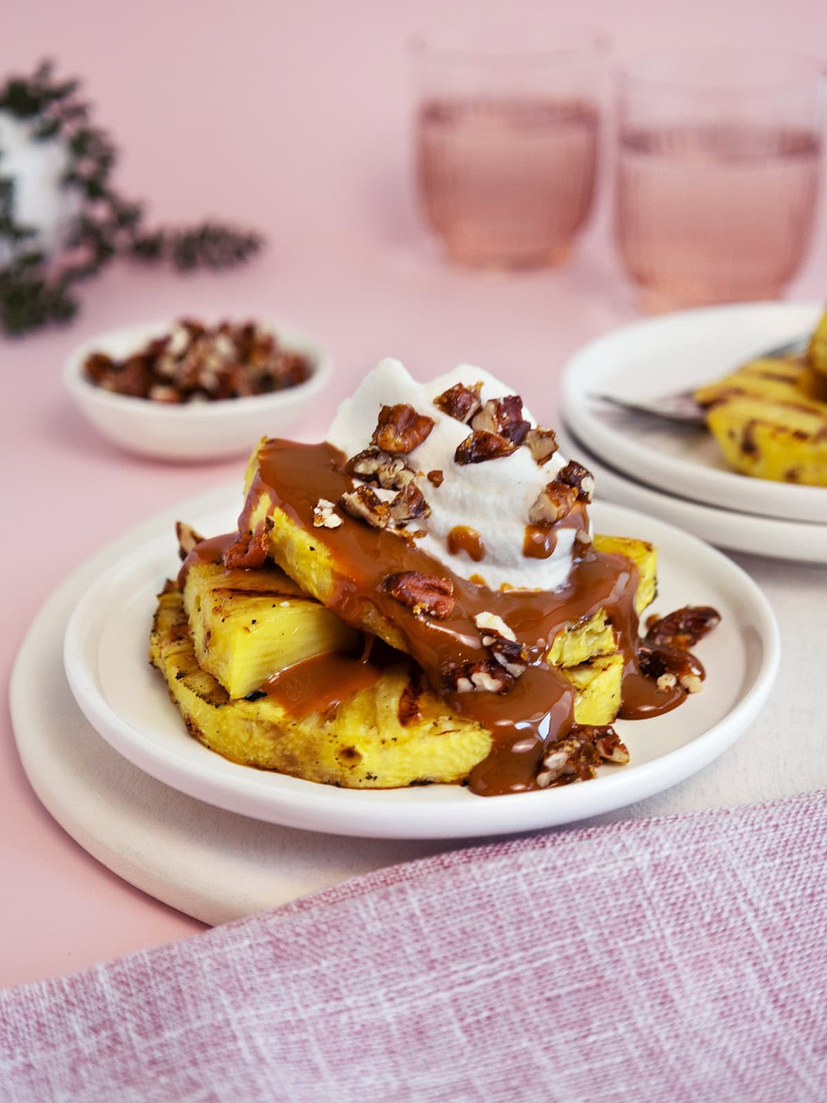 Grilled pineapple on a white plate that's topped with caramel sauce and whipped cream.