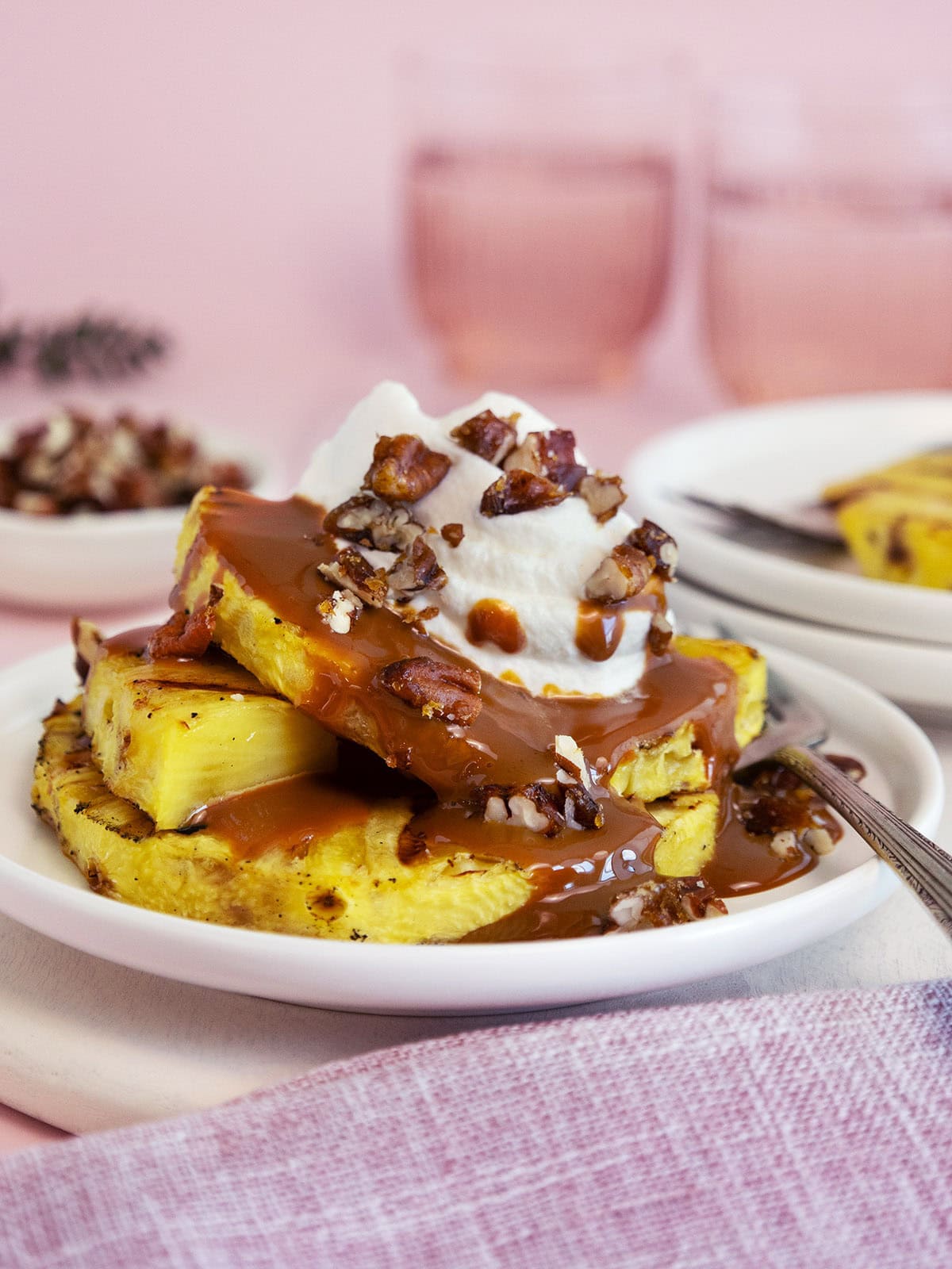 Close up of grilled pineapple on a white plate topped with caramel and whipped cream.