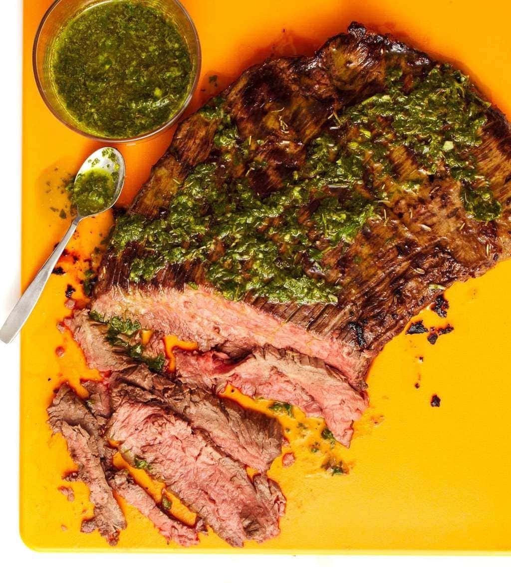 grilled flank steak on a yellow cutting board with salsa verde