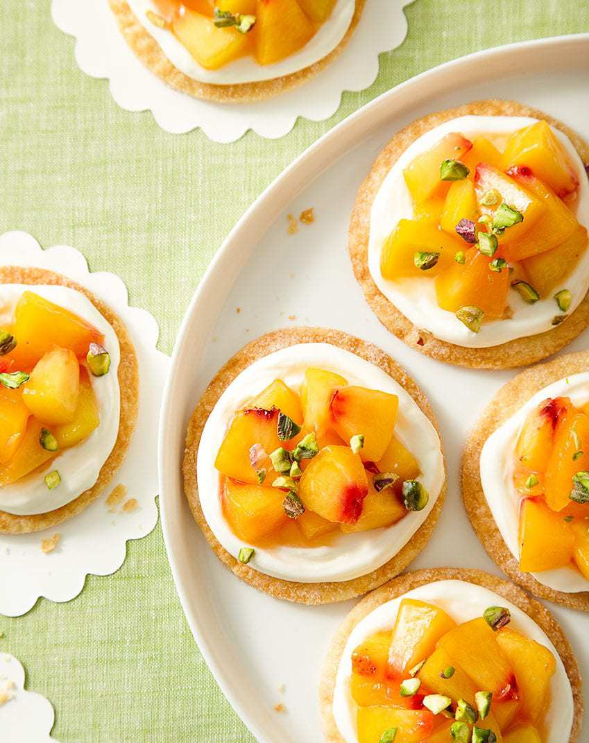 Fresh peaches on top of pie crust with cream on white platter and green linen