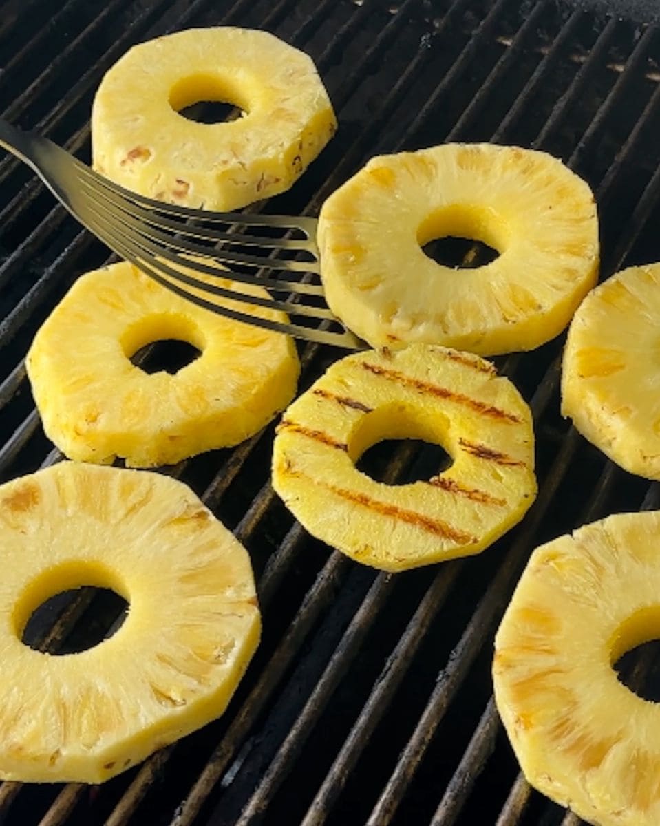 Pineapple slices on a grill with a slice being flipped.