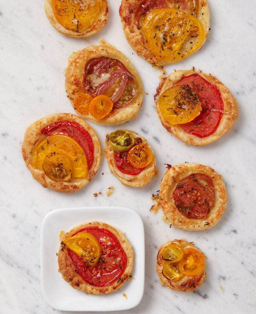 Mini tomato tarts with puff pastry on white marble and small white plate