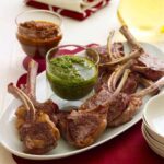 baby lamb chops on white plate with green and red sauces