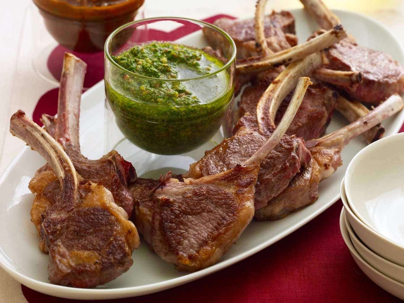 Lamb Chops with red and green sauce on oval white plate, red linen