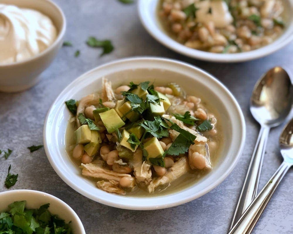  a bowl of Chicken Chili Verde in white bowl w spoons