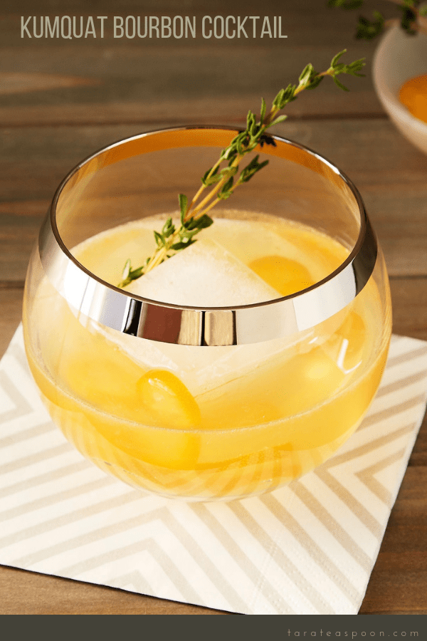 Glass of a Thyme Cocktail with kumquat and bourbon on striped cocktail napkin