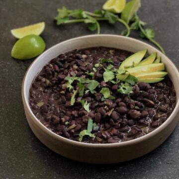 creamy black beans in a bowl with cilantro, lime and avocado fixings
