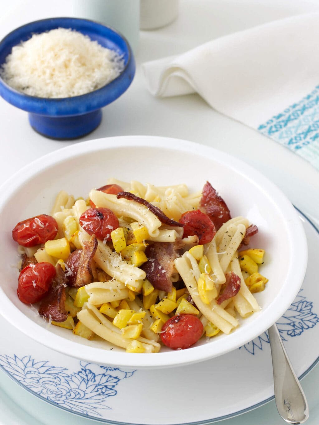 Pasta with yellow squash and tomatoes in white bowl