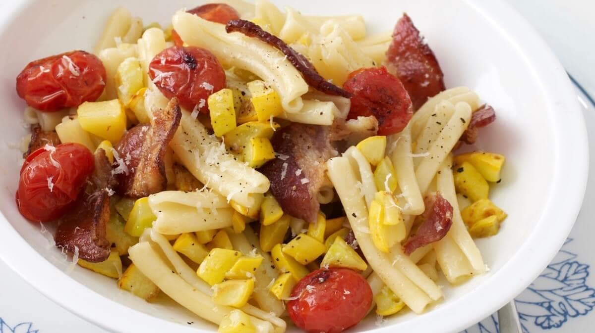 pasta with tomatoes bacon and yellow squash on blue plate