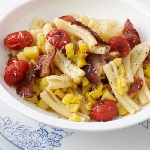 Pasta with tomatoes, bacon and yellow squash in white bowl