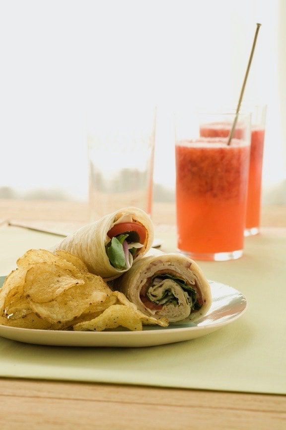 Turkey wraps and chips with lemonade on yellow linen