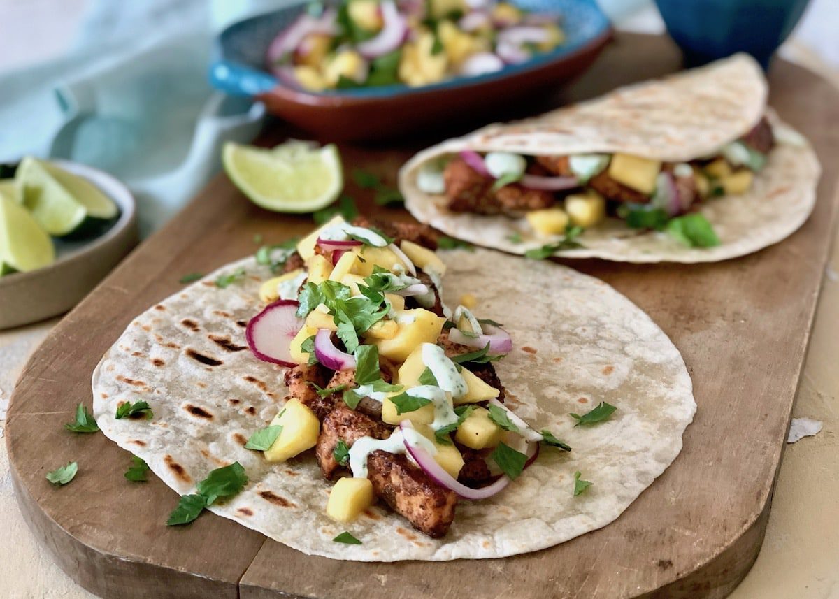 tacos with lime wedges and salsa in the background on cutting board