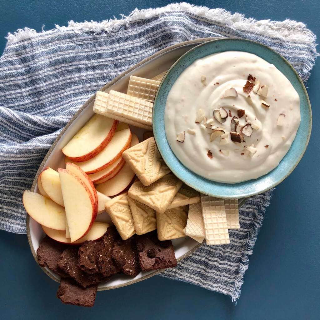 Fruit dip with apples and cookies on blue linen and blue surface