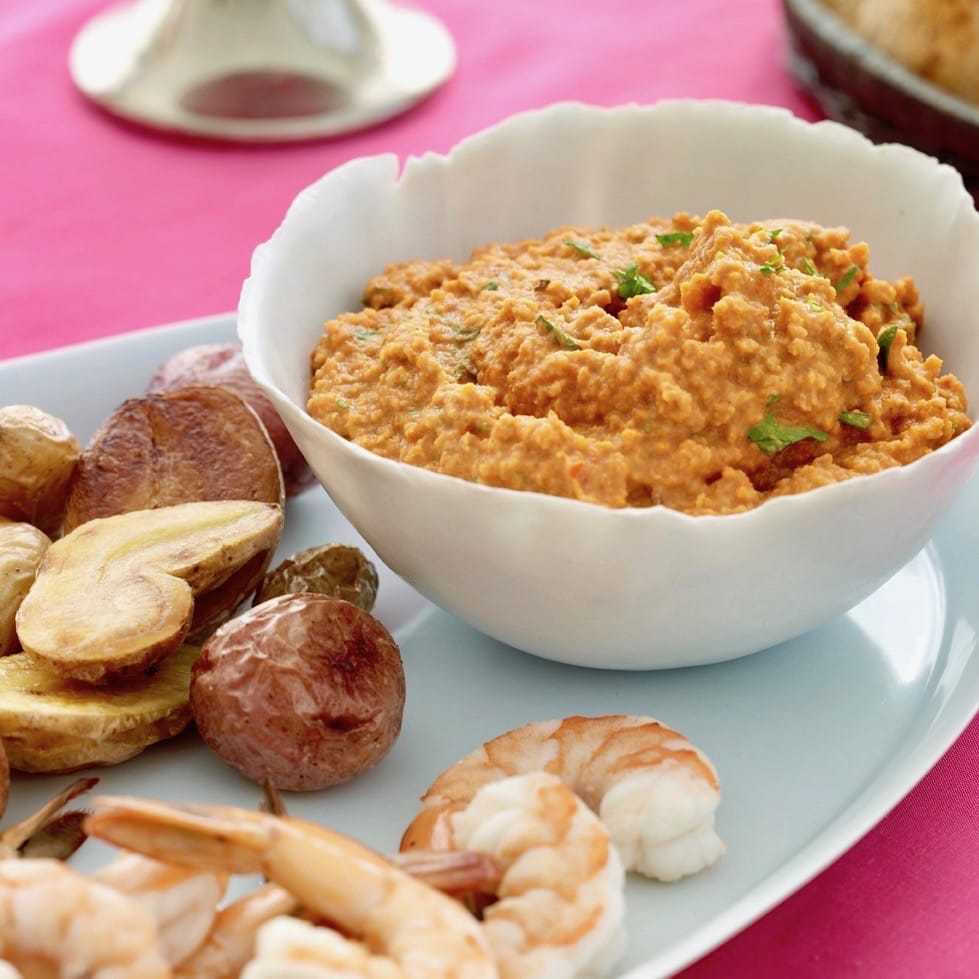 Romesco dip in a white bowl with shrimp and potatoes