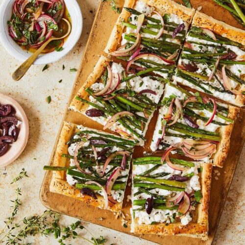 asparagus tart cut into squares with bowl of red onion dressing