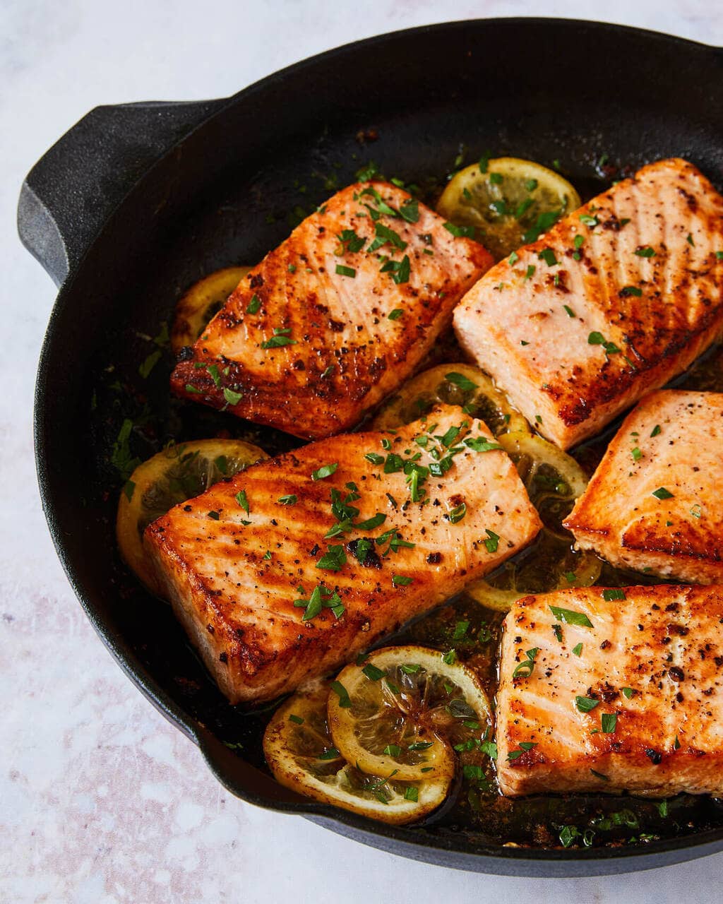 salmon cooking in a cast iron pan with lemon and herbs