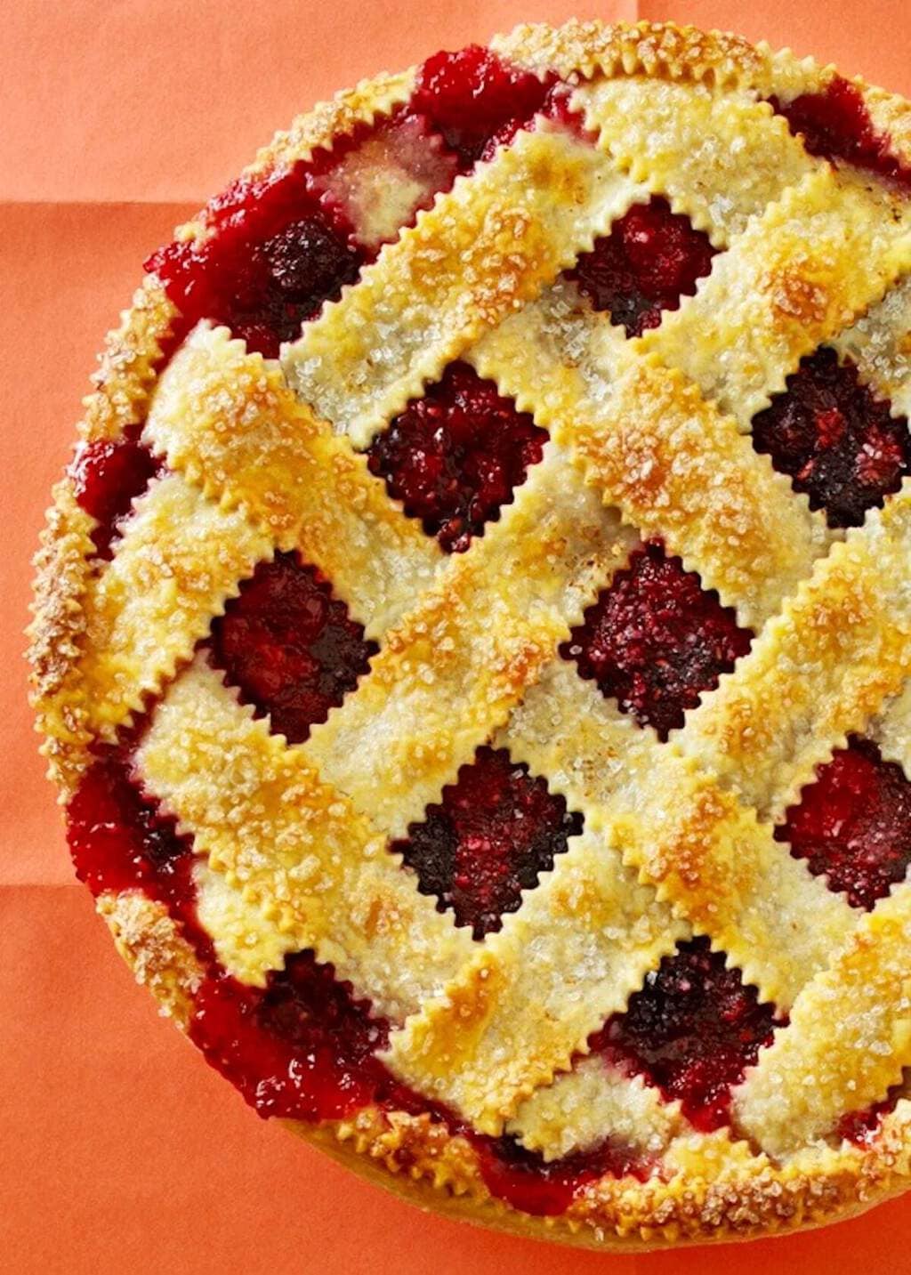 overhead view of a lattice top razzleberry pie on orange paper