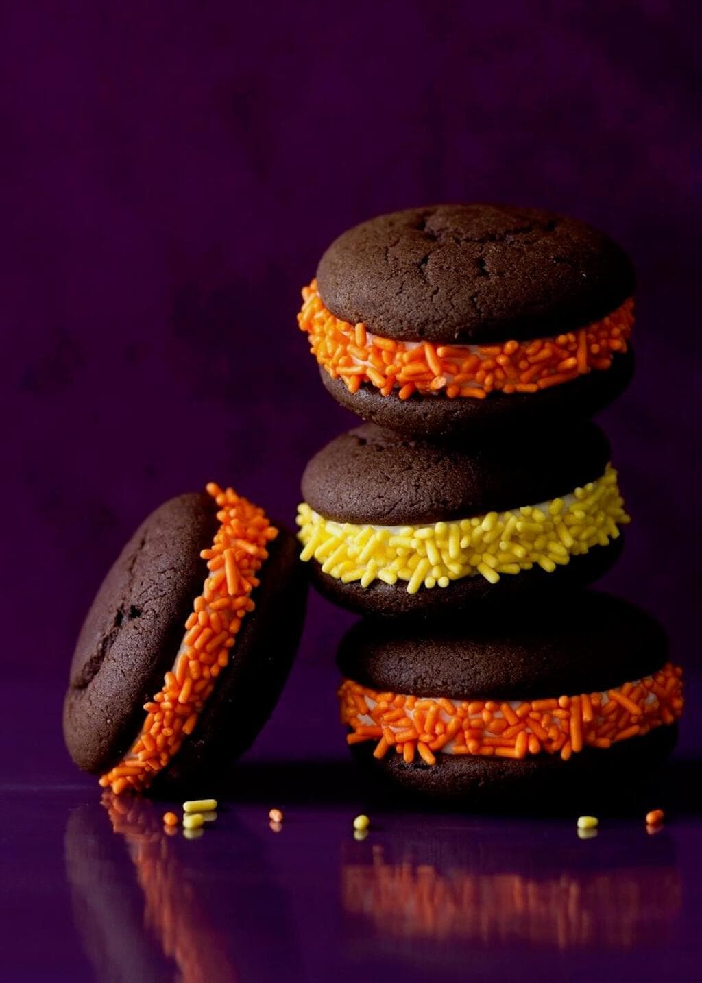 Chocolate whoopie pies with orange and yellow frosting, rolled in sprinkles to match