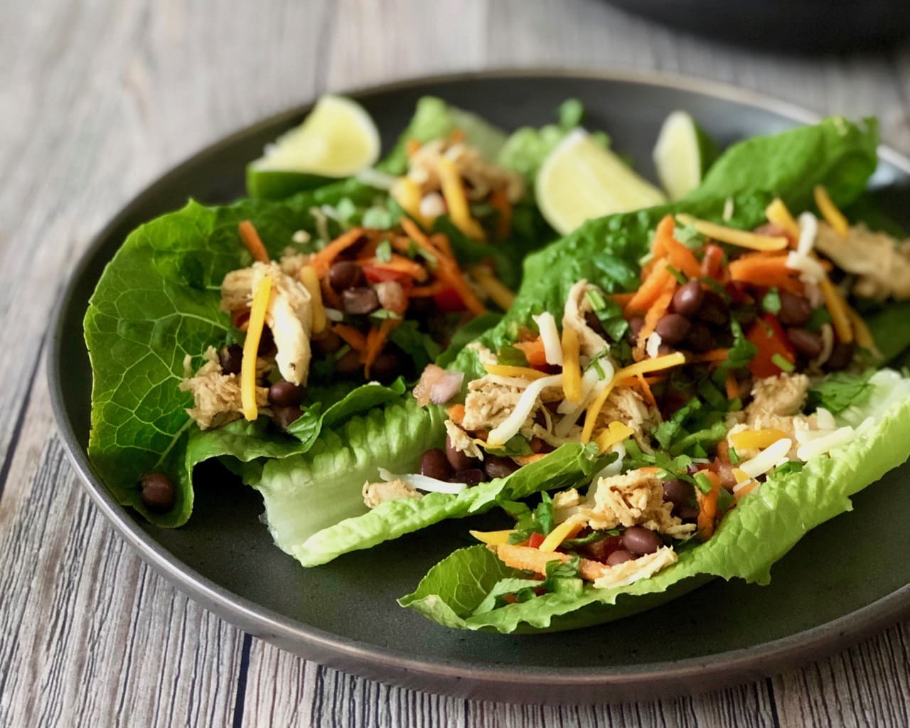 Healthy Taco Salad Lettuce Wraps on a plate with black beans chicken and slices of lime