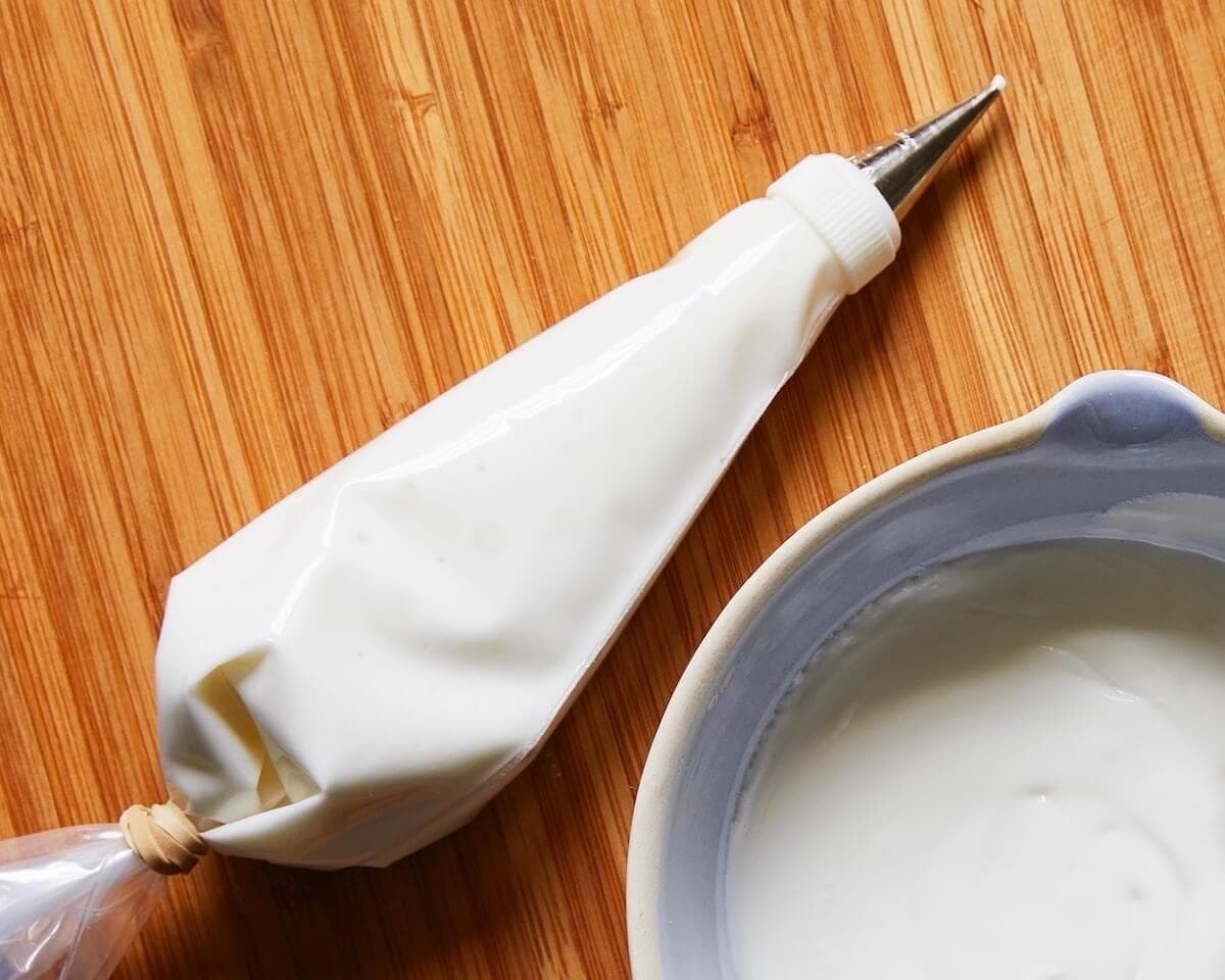White Royal Icing in a piping bag next to a bowl of icing